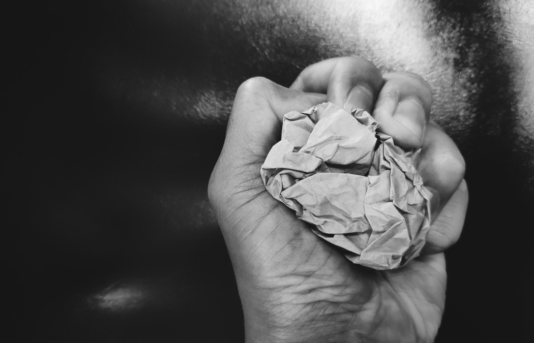 A hand tightly gripping a crumpled piece of paper against a dark background.