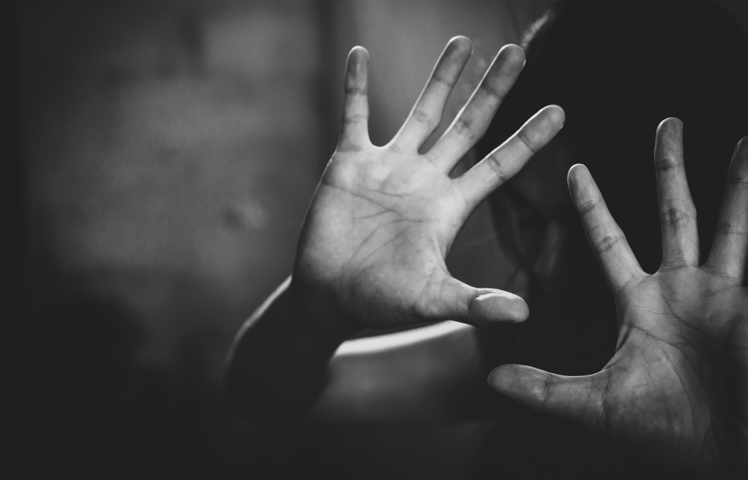 A person holding up both hands in front of their face, palms facing outward, with a dark and blurred background.