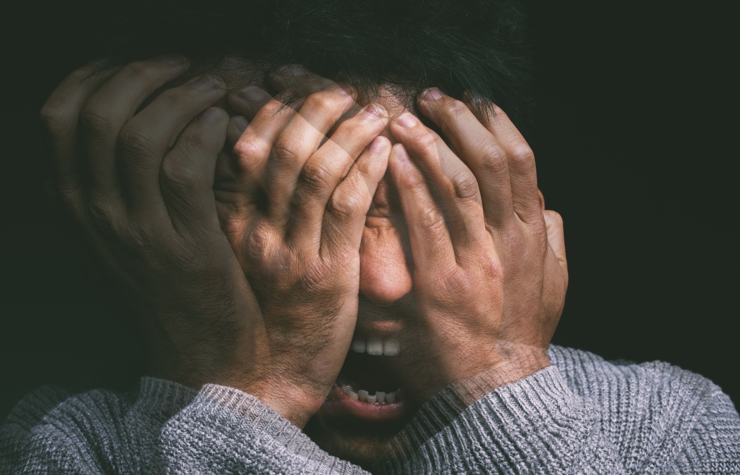 A person with hands covering their face, appearing distressed, with a double exposure effect emphasizing emotional intensity.