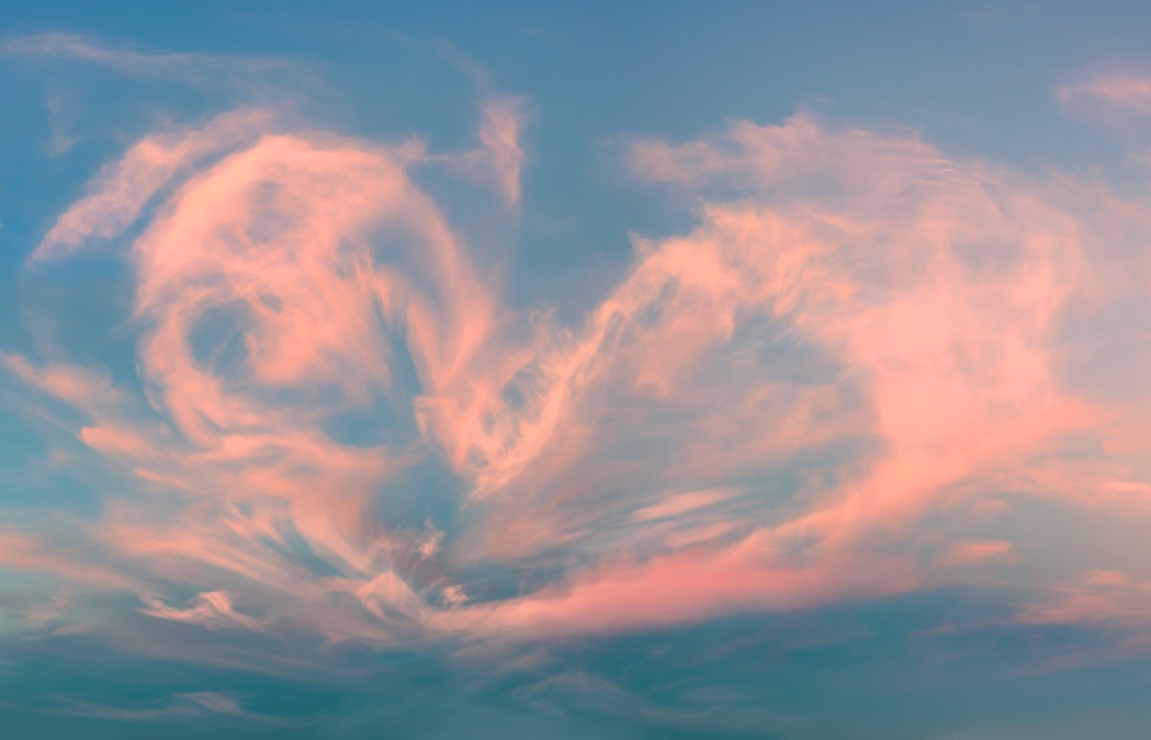 Pink and orange clouds are illuminated by soft sunset light against a blue sky, creating delicate, wispy patterns in the atmosphere.