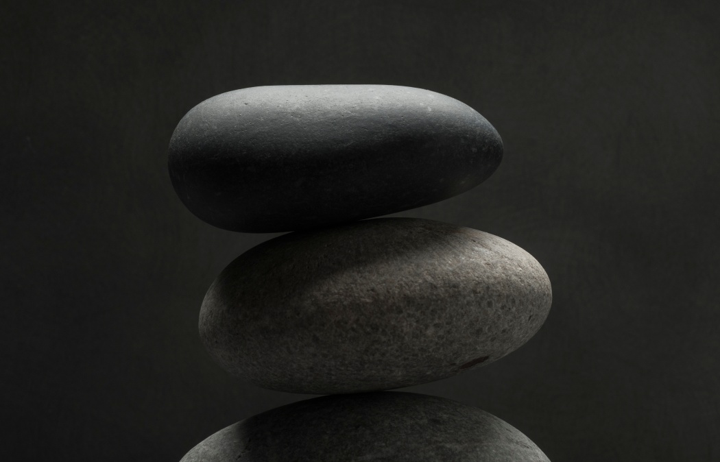 Two smooth, oval stones stacked on top of each other against a dark, plain background.