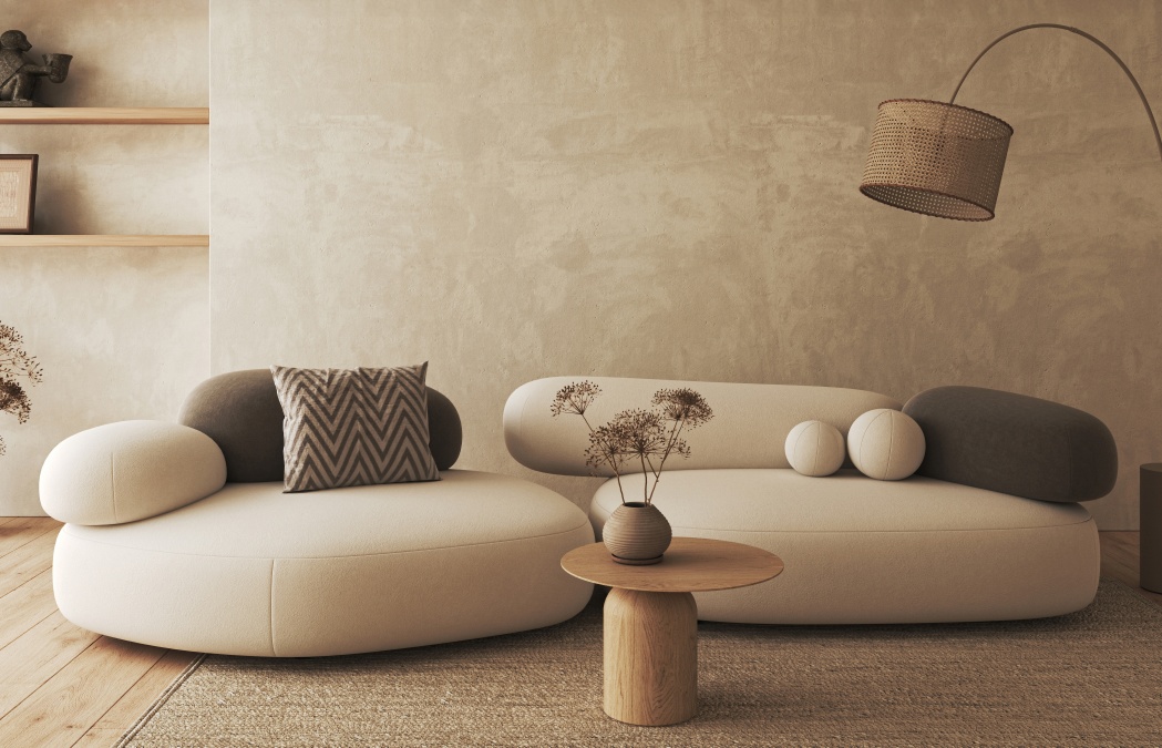 Modern living room with rounded cream and gray sofas, a small wooden table with dried flowers, and a woven floor lamp against a beige textured wall.