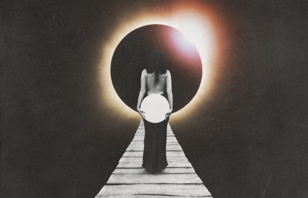 A person stands on a wooden path holding a glowing sphere, facing a solar eclipse with a dark sky in the background.
