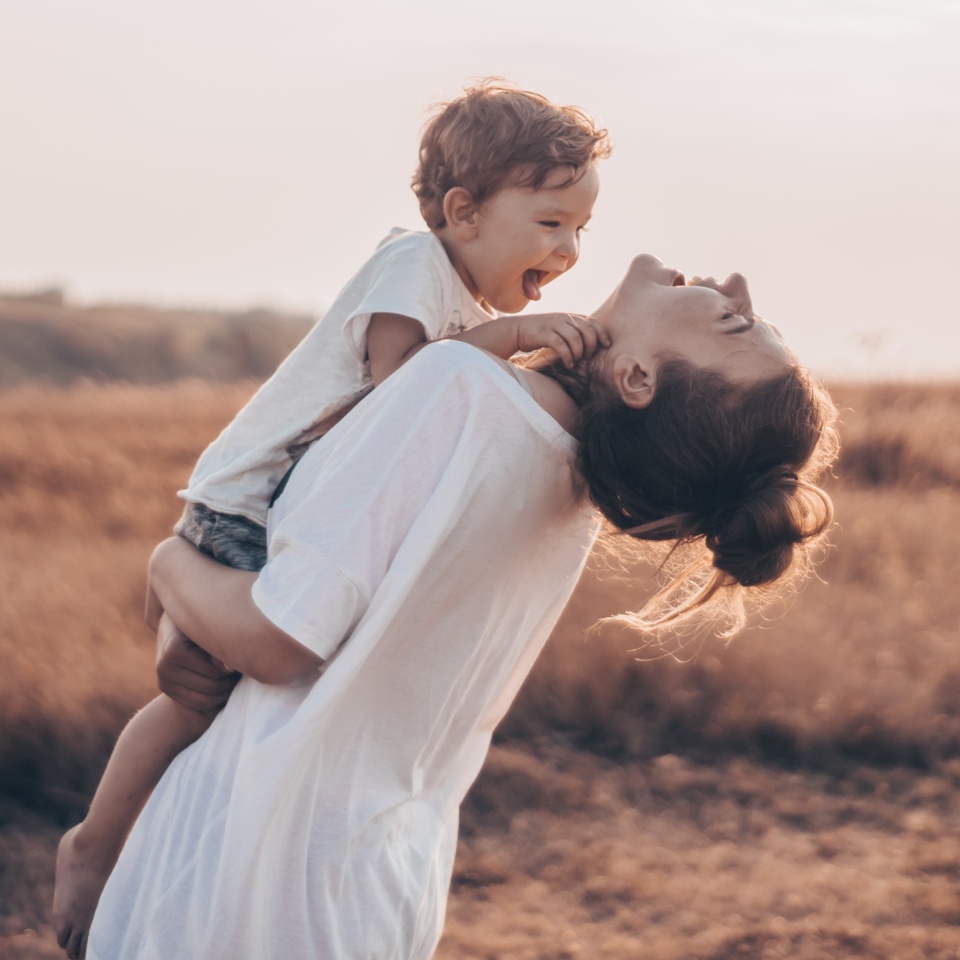 Young woman kisses her little son at sunny in the meadow in sunset. Young mother holding her baby. Mother and little son having good time in the nature. Color toned image. Mothers Day. Family Concept