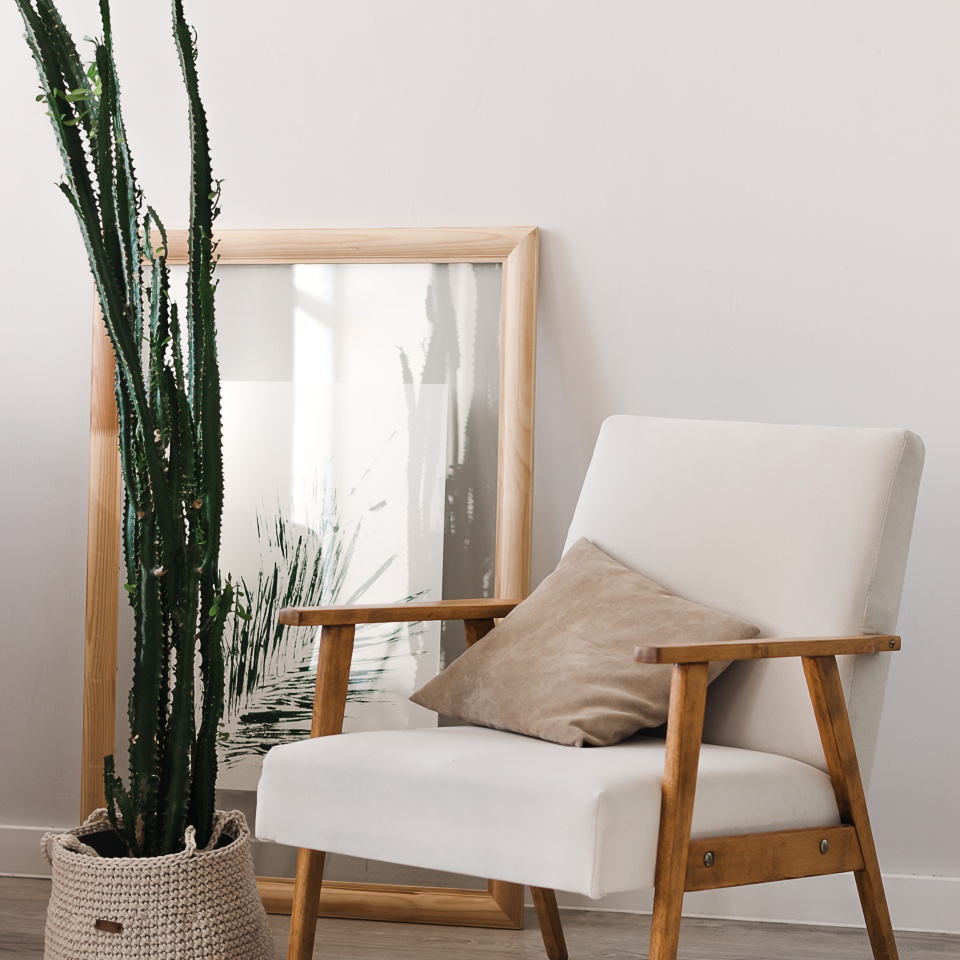 A fragment of a home interior.A light chair,a picture, and a houseplant on the light floor.Minimalistic style.