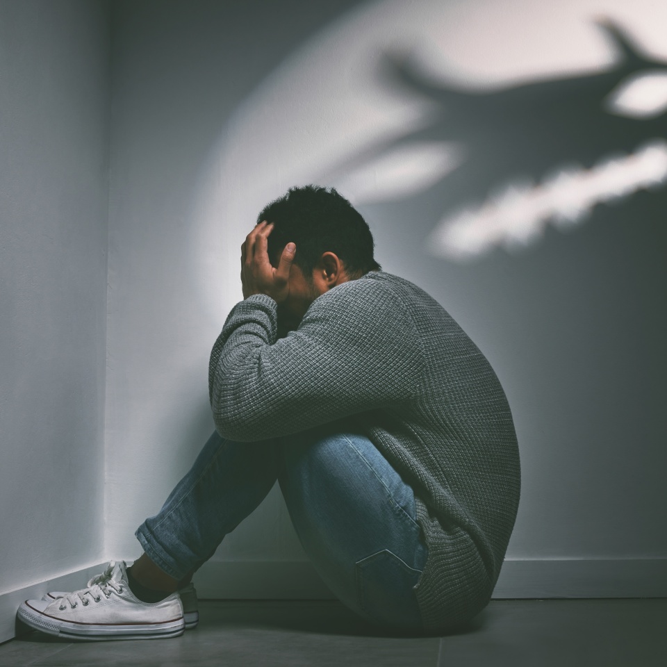 If dreams come true, can nightmares too. Shot of a young man sitting in the corner of a dark room with a scary figure on the wall.