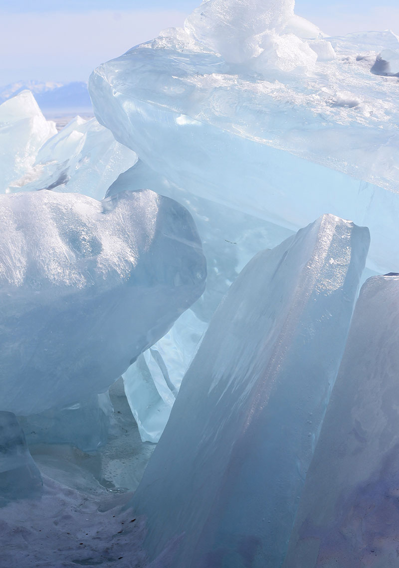 Large, translucent blue ice slabs stacked together, with smooth and jagged surfaces, under a pale sky.