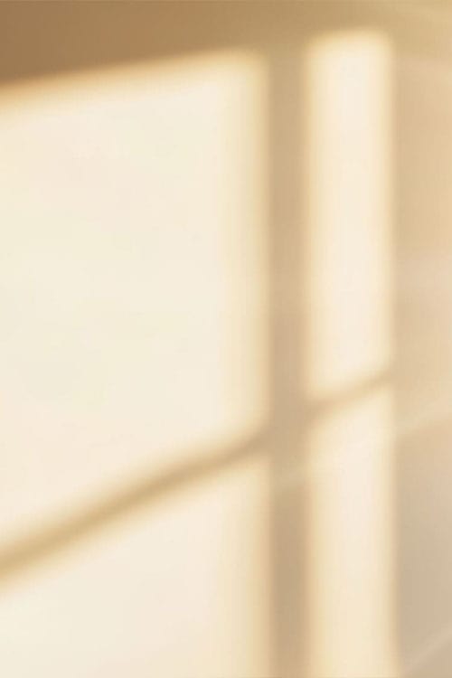 Soft sunlight casts the shadow of a window frame on a beige wall.